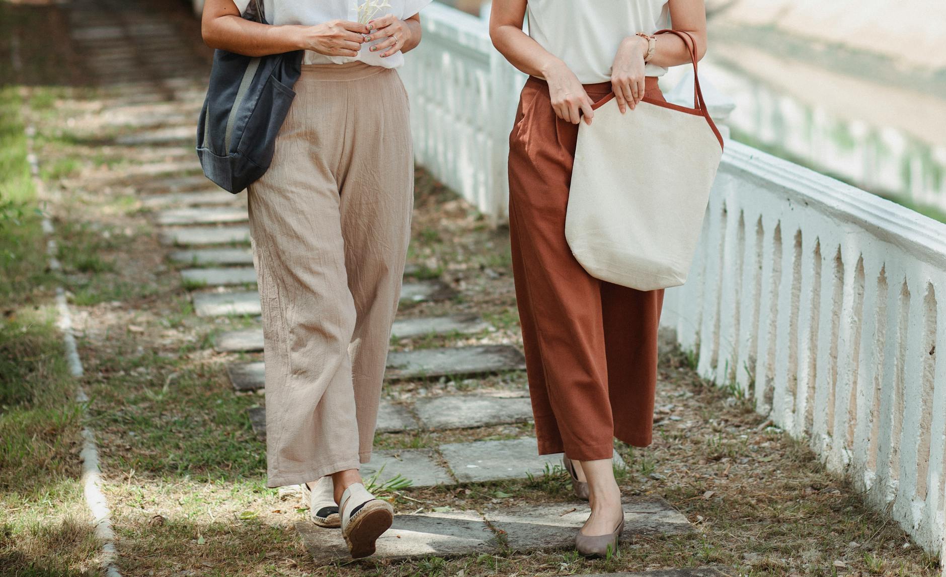 faceless female friends walking on pathway in city
